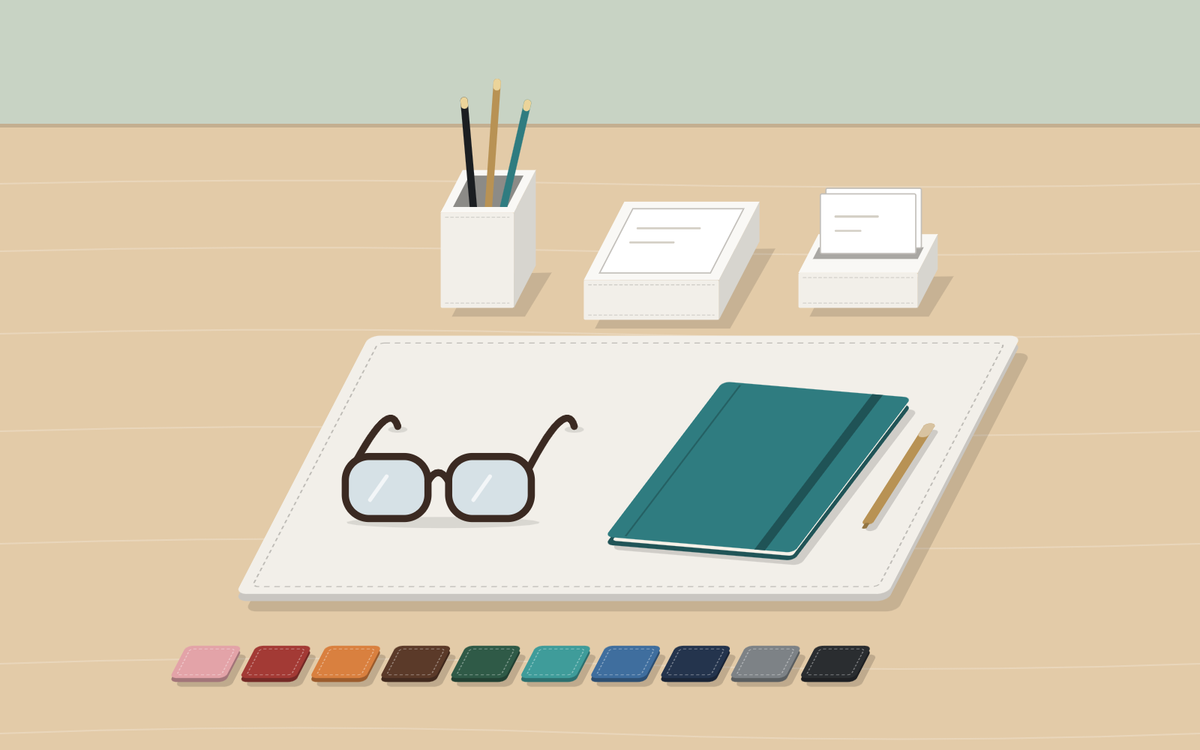 Illustration: a light wood desk seen from slightly above with a white desk pad, pen cup, memo holder and card holder, a row of color swatches, and glasses, a closed notebook and a pen on the pad