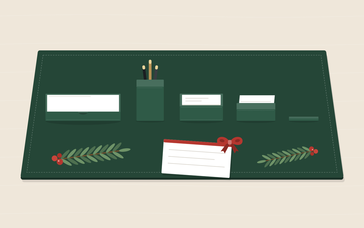 Illustration: a green desk pad with a document tray, a pen cup, a memo holder and a card holder, two pine sprigs with red berries and a note card tied with a red bow