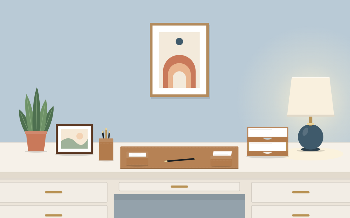 Illustration: a white office desk seen from the front with a tan desk set, a small potted plant, a framed picture and a table lamp, and one framed print on the blue wall behind